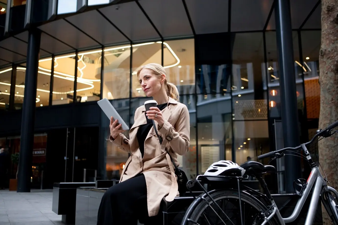 Mujer trabajando en su tableta al aire libre y bebiendo café.